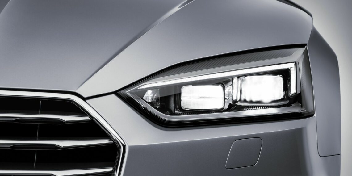 Close-up of a lit Audi Matrix LED headlamp on a silver car, studio background