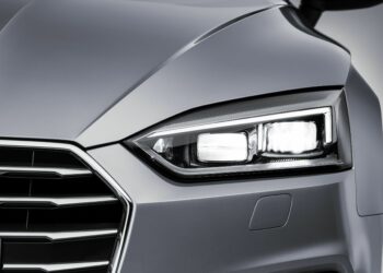 Close-up of a lit Audi Matrix LED headlamp on a silver car, studio background