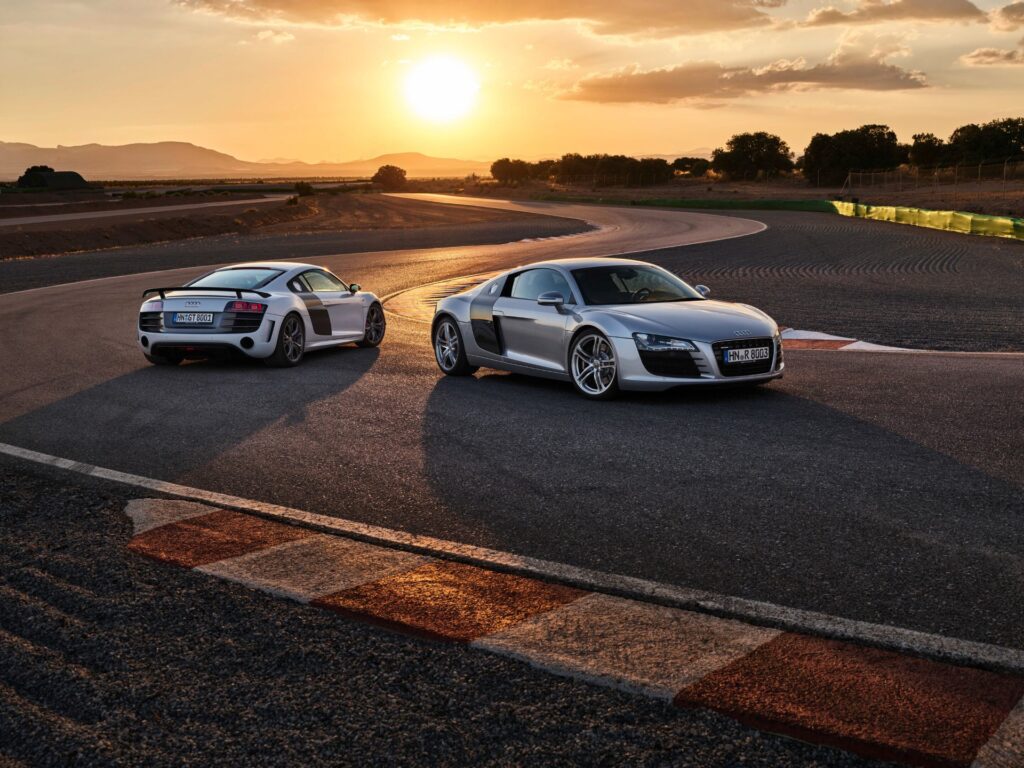 Two first-generation Audi R8 coupes on a racetrack at sunset