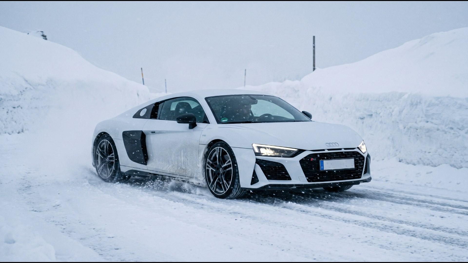 White Audi R8 V10 driving between snowbanks on a winter mountain pass