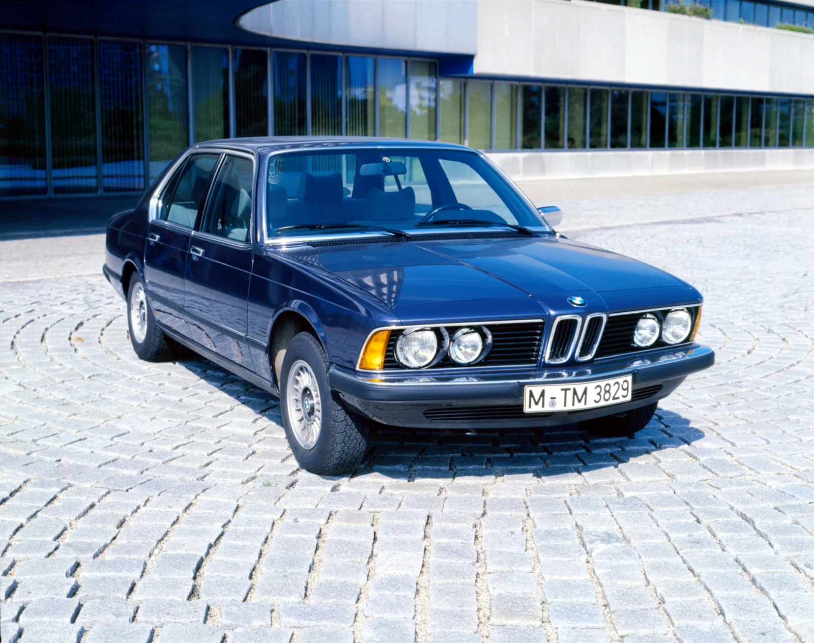 Dark blue BMW 7 Series E23 sedan with four round headlights parked on cobblestones