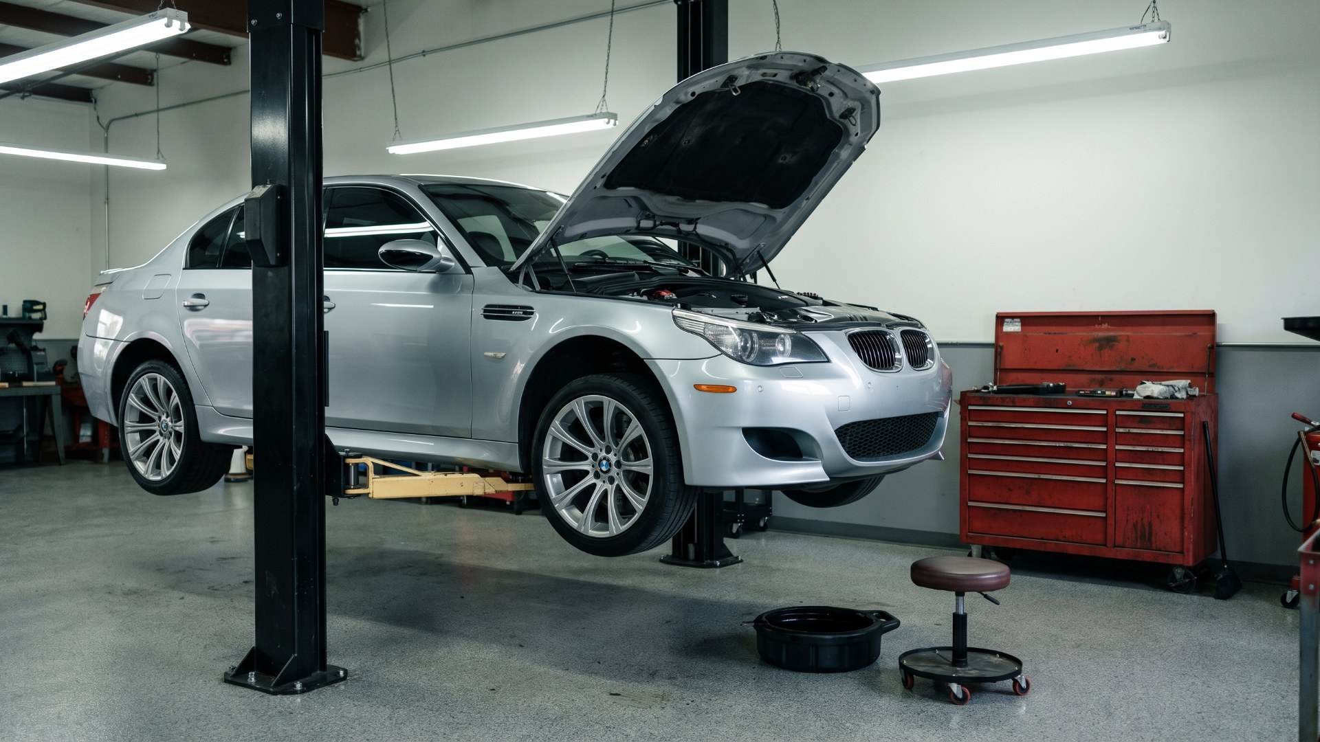 Silver BMW E60 M5 raised on a two-post lift with its hood open in a repair shop