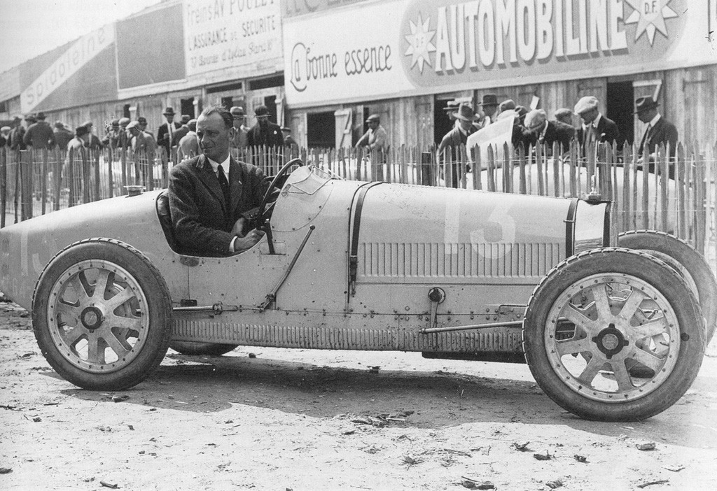 Black-and-white 1924 photograph of a driver seated in a Bugatti Type 35 racing car in the pits at the Grand Prix in Lyon