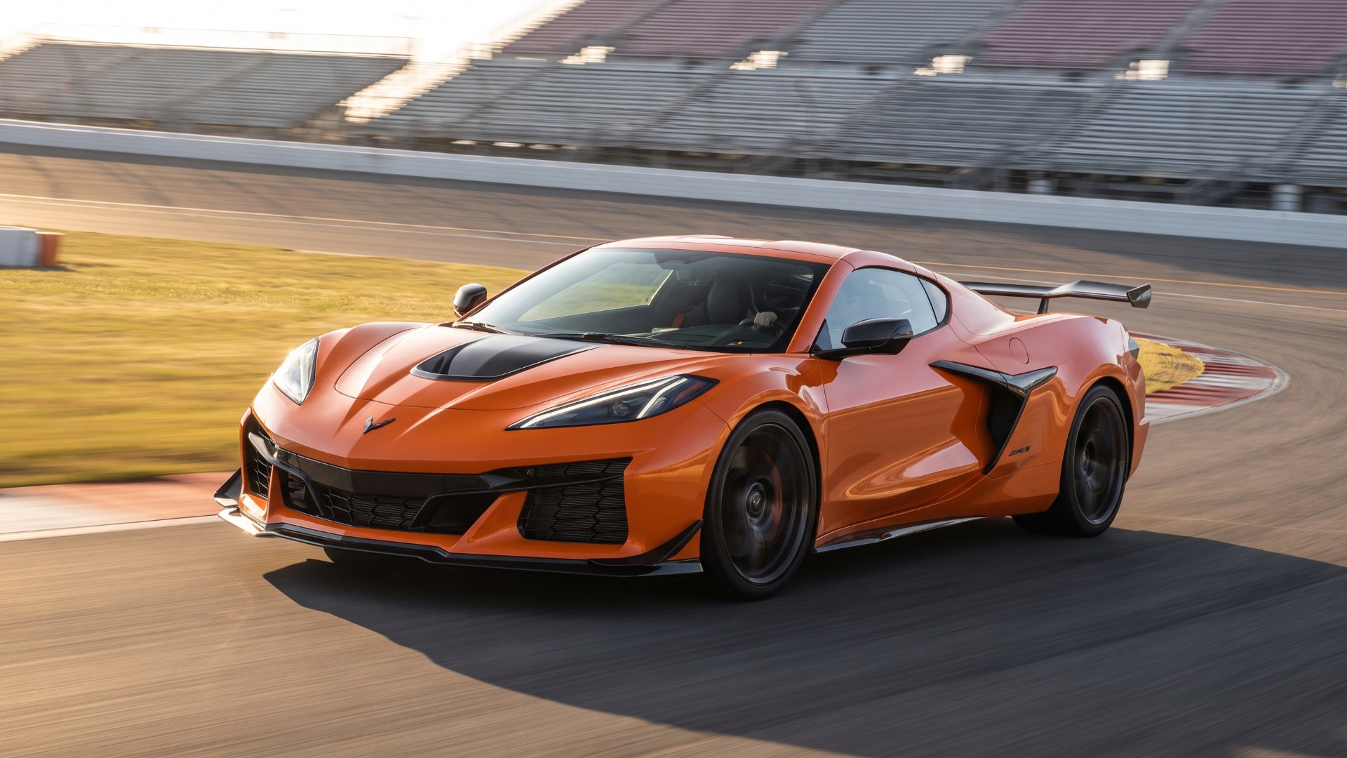 Orange Chevrolet Corvette ZR1X with a carbon rear wing cornering on a racetrack in front of empty grandstands