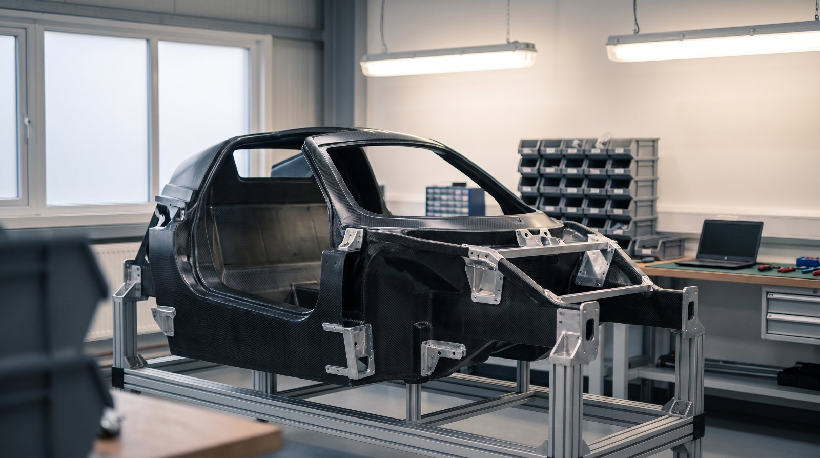 Illustration of a bare carbon-fiber supercar monocoque on a workshop assembly stand