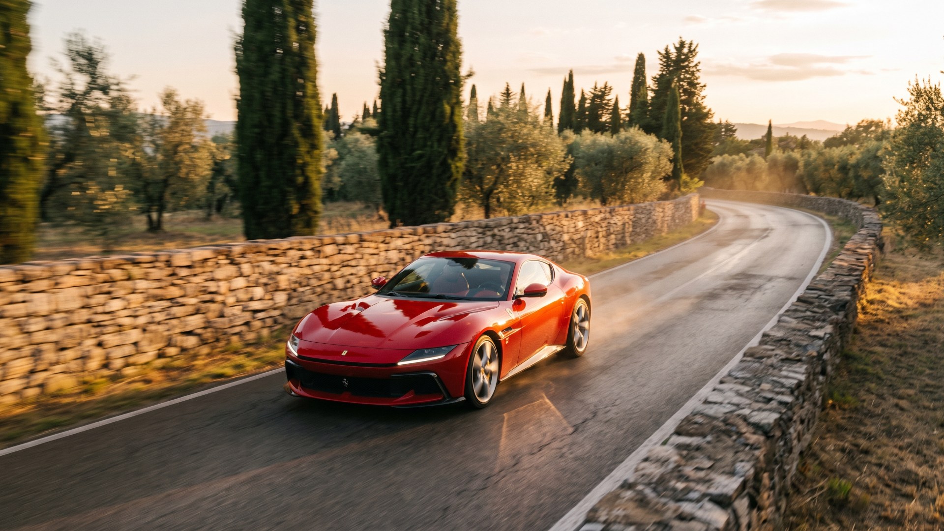 Red Ferrari 12Cilindri driving on a winding road between stone walls and cypress trees at sunset