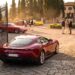 A dark red Ferrari Roma waits at open estate gates while owners gather around classic and modern Ferraris in the courtyard beyond