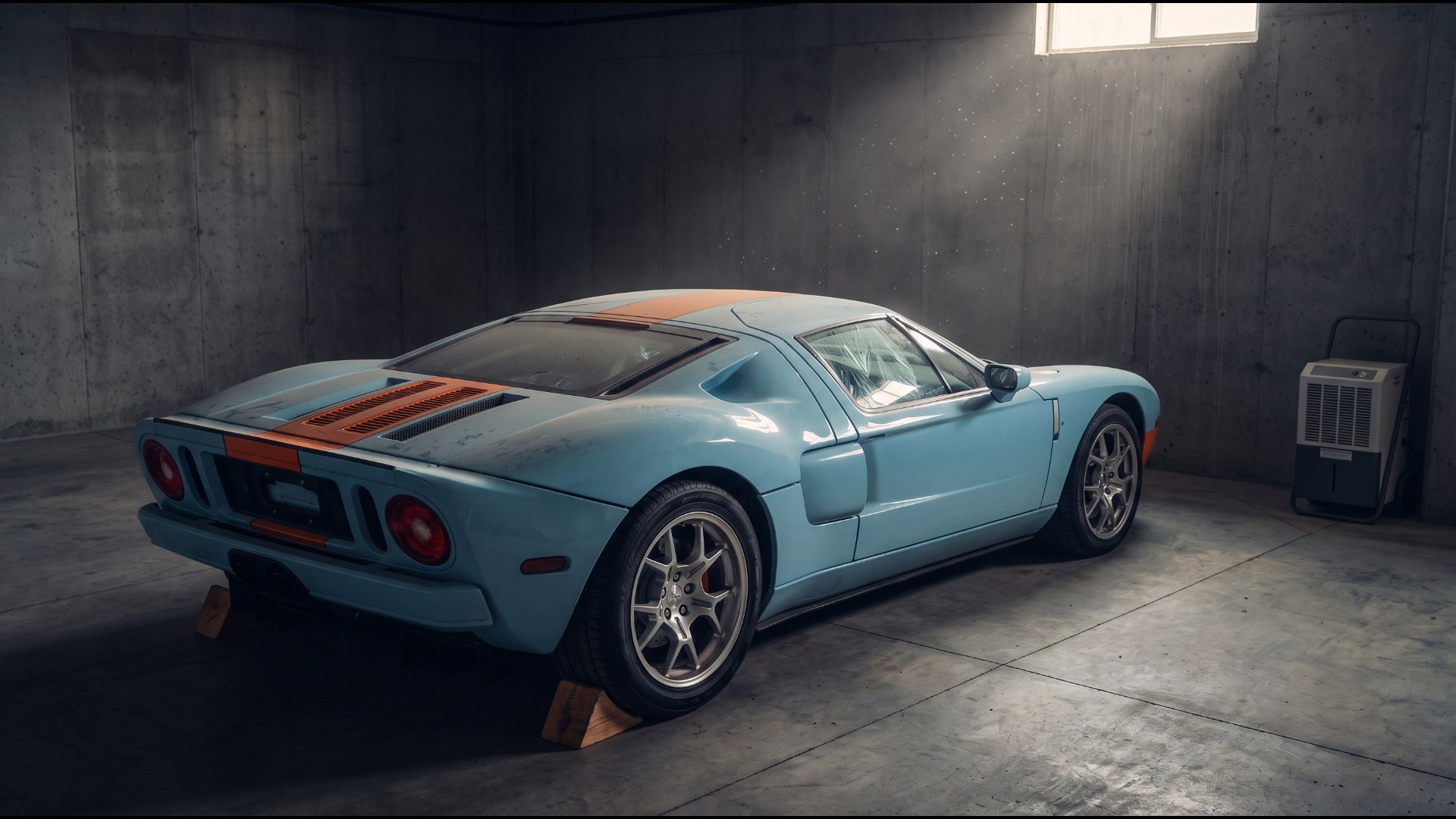 Light blue Ford GT with an orange center stripe stored on wheel chocks beside a dehumidifier, the way many low-mileage supercars are kept