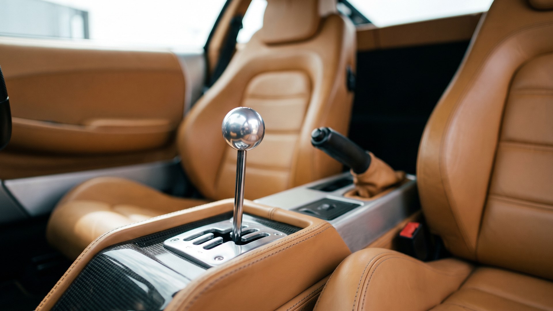Open-gate six-speed manual shifter with a polished ball knob in a tan leather sports-car interior