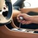 Driver’s hand on a polished aluminum gear knob above an open metal shift gate in a tan leather cabin