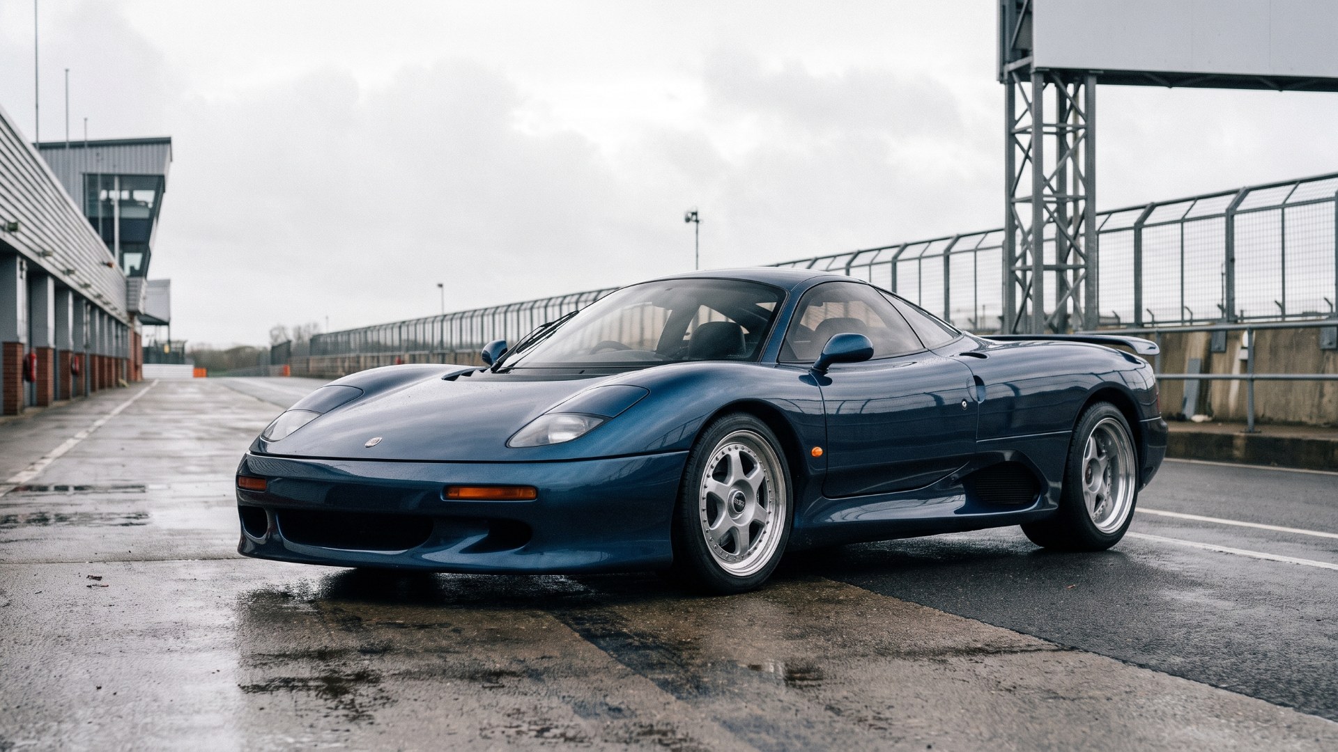 Dark blue Jaguar XJR-15 parked on a damp racing-circuit pit lane