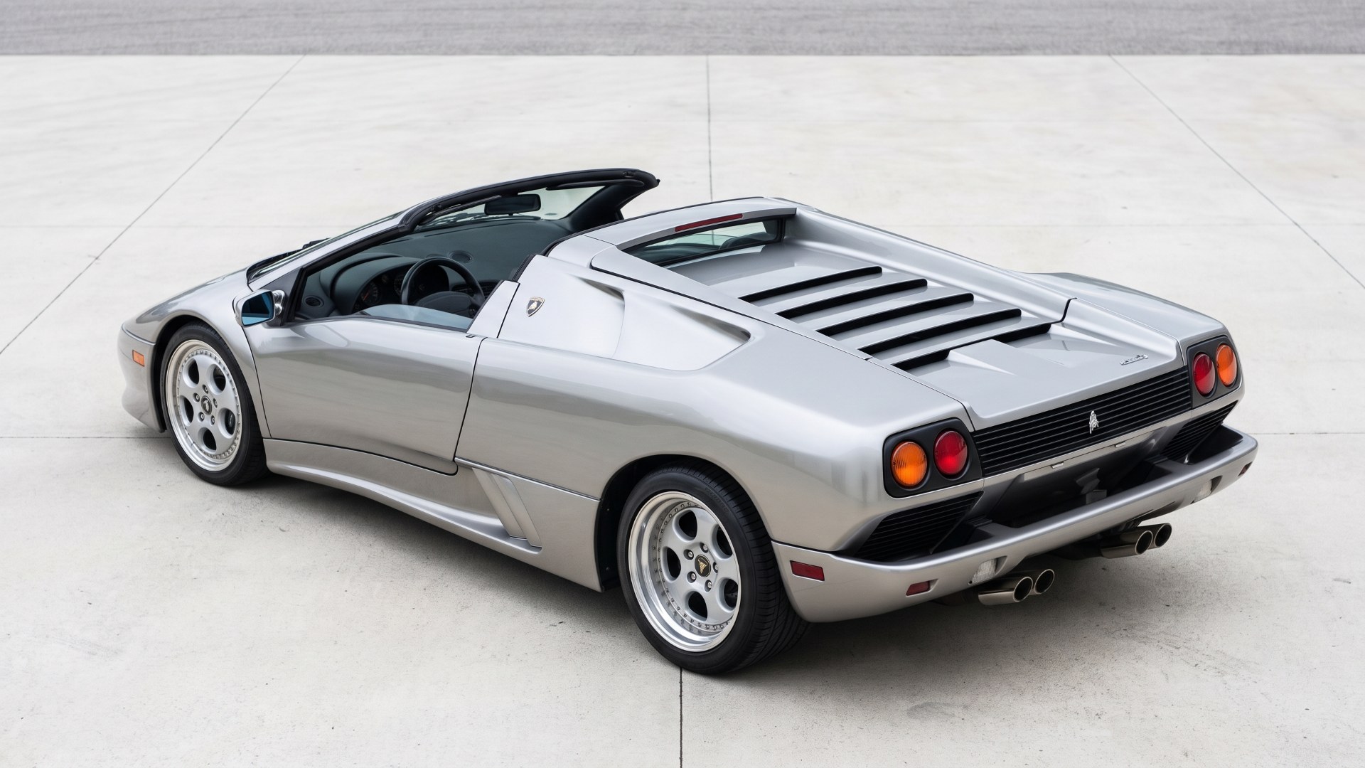 Rear three-quarter view of a silver Lamborghini Diablo VT Roadster showing the slatted engine cover and round tail lamps