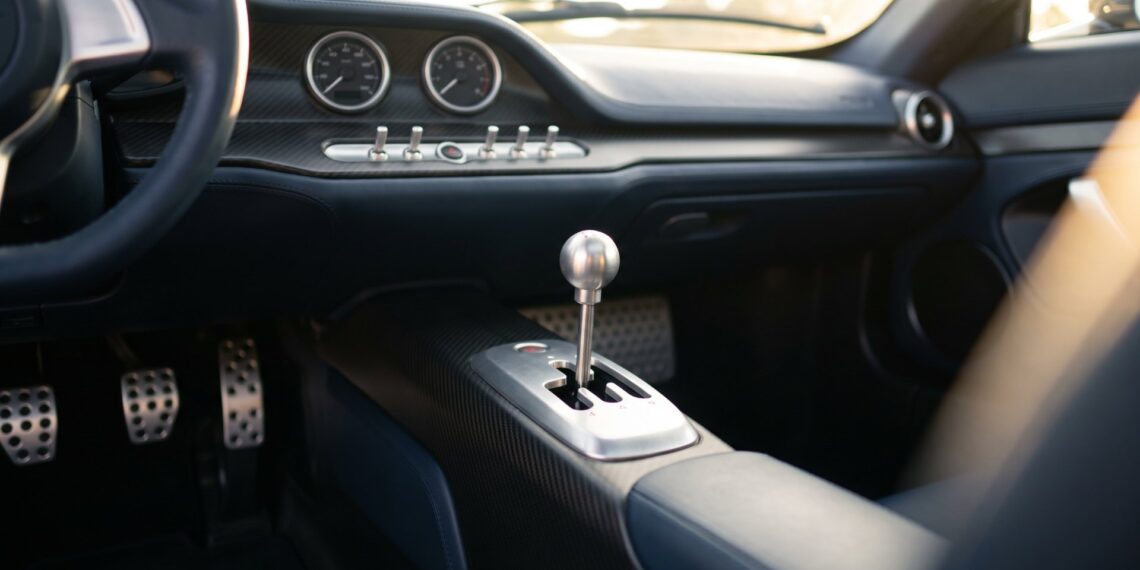 Illustration of a polished metal gear lever in an open gate and three drilled pedals in a minimalist hypercar cabin with two analog gauges