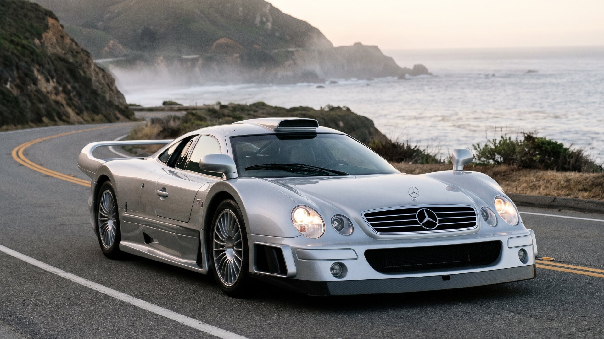 Silver Mercedes-Benz CLK GTR Straßenversion road car on a coastal road at dawn, front three-quarter view, editorial illustration