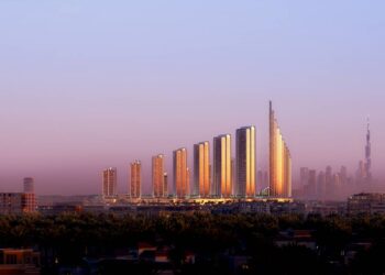 Rendering of the planned Mercedes-Benz Places Binghatti City masterplan: twelve gold-lit towers rising in a graduated line to a tall spiraling tower, with the Dubai skyline and Burj Khalifa in the distance at dusk
