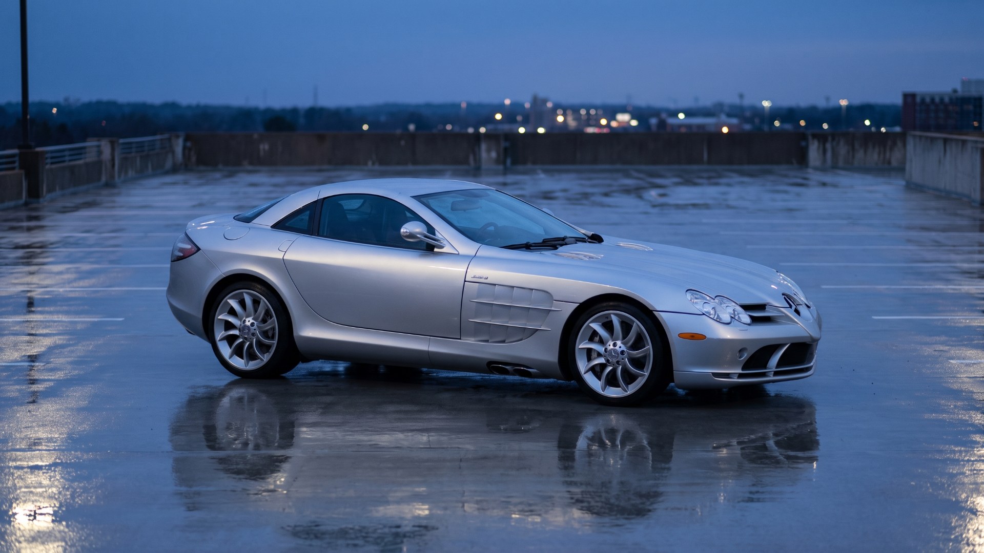 Silver Mercedes-Benz SLR McLaren coupe parked on a rooftop parking deck at dusk