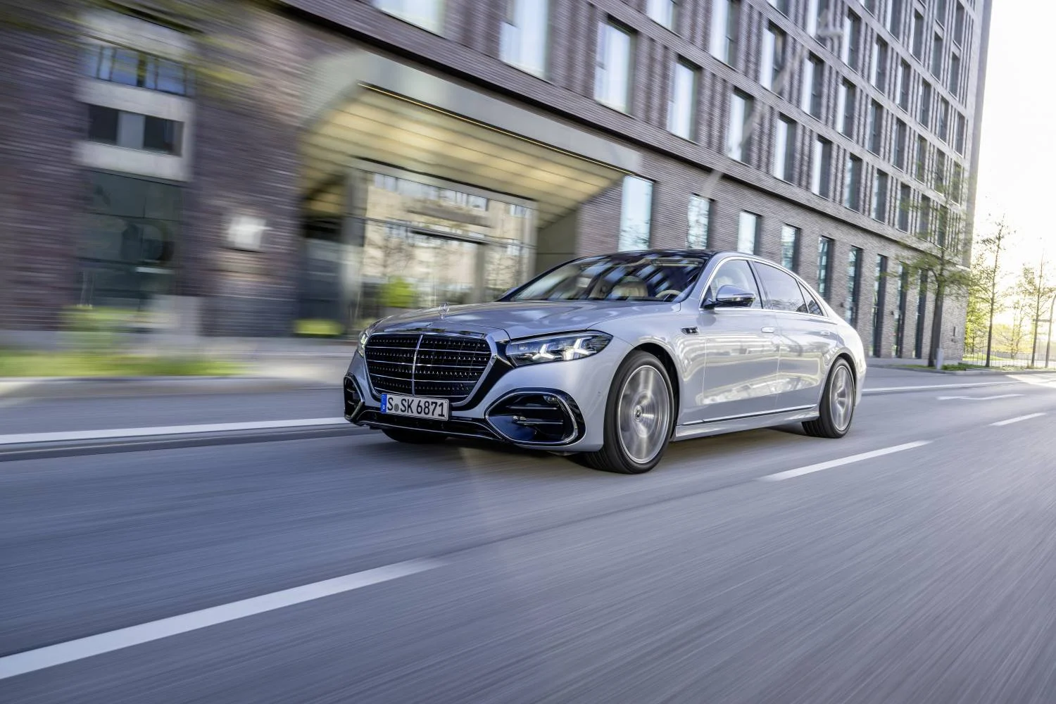 Silver 2026 Mercedes-Benz S-Class driving past a modern office building