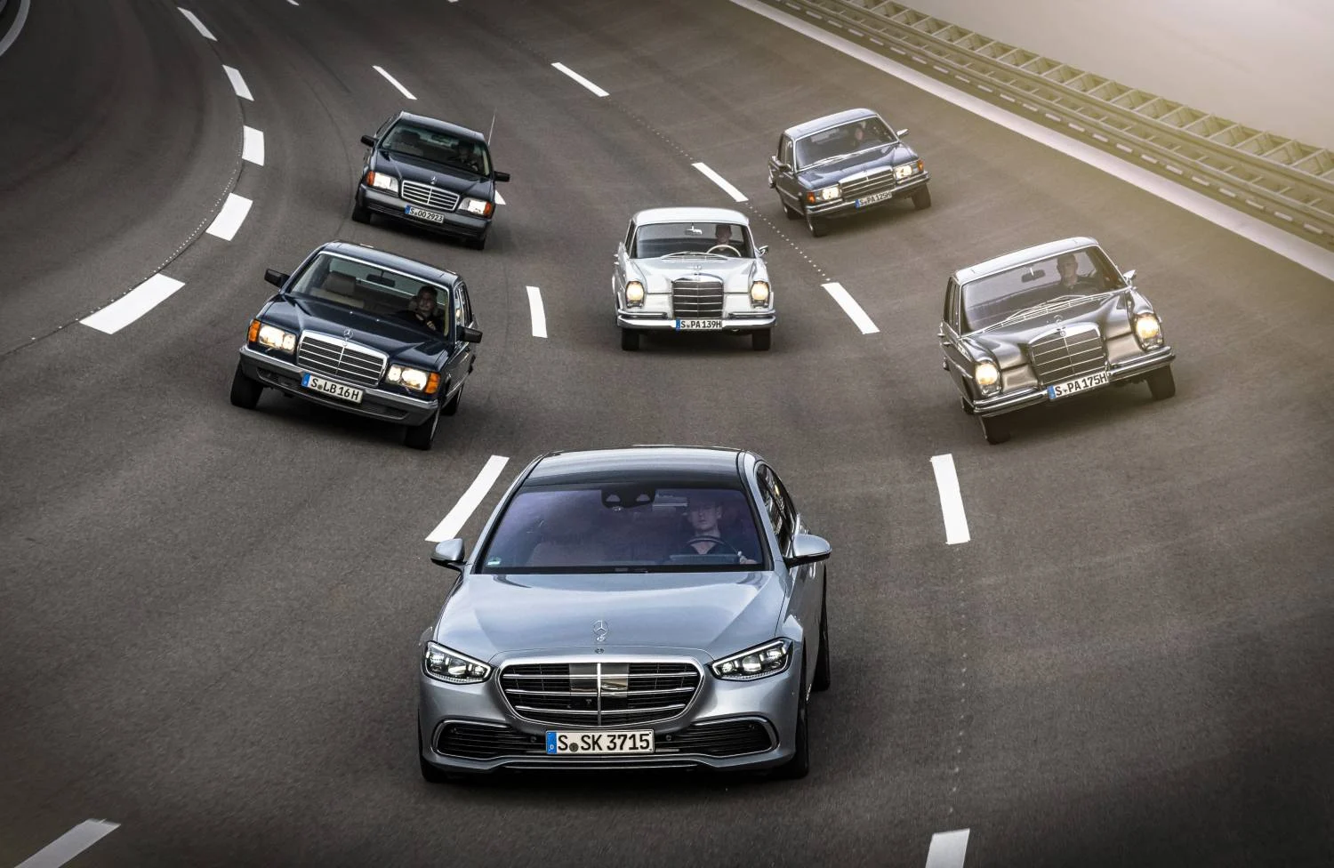 A silver 2020 Mercedes-Benz S-Class leads older S-Class generations around a curve on a test track