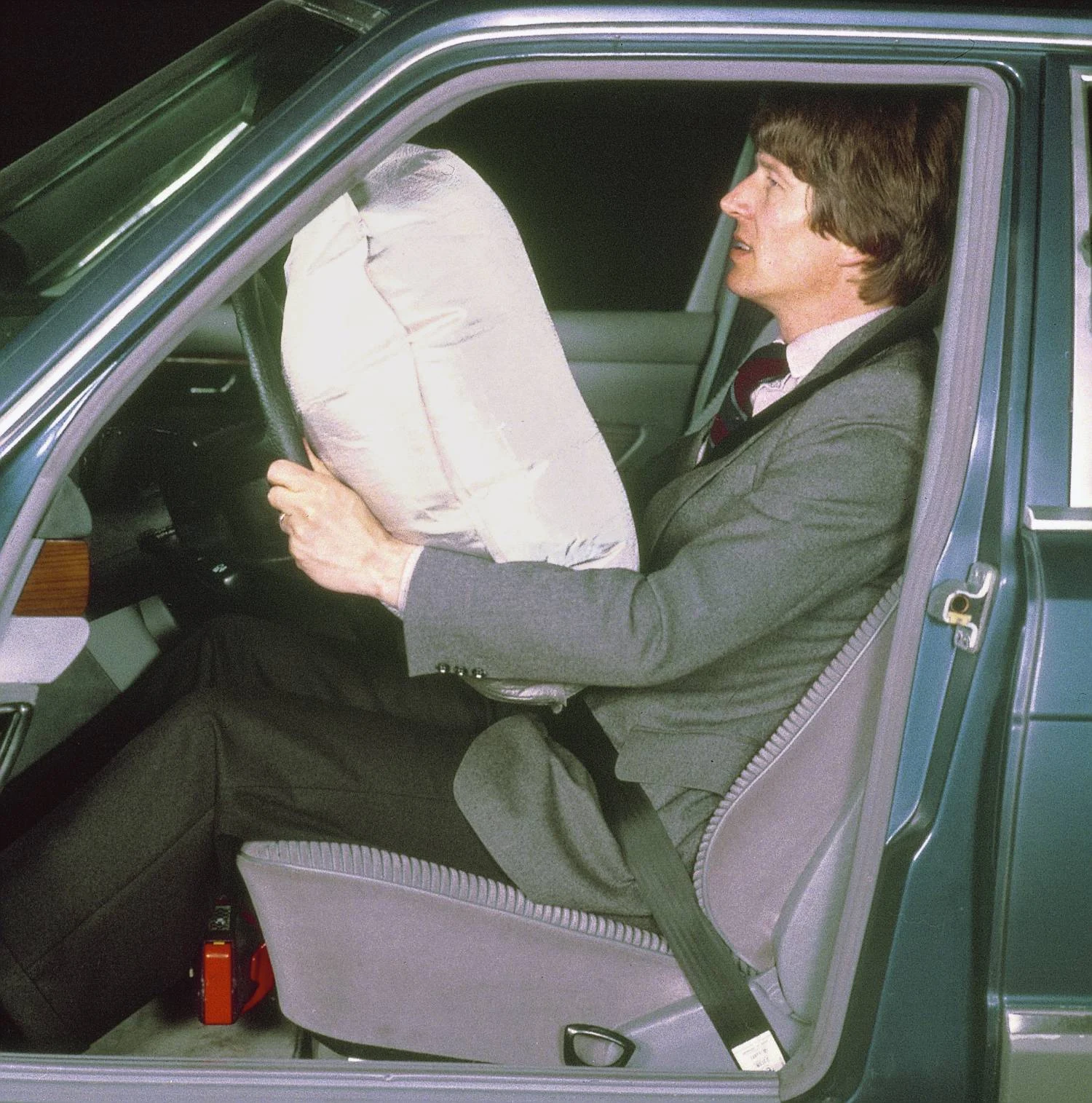 A driver seated in a Mercedes-Benz W126 with the steering-wheel airbag inflated