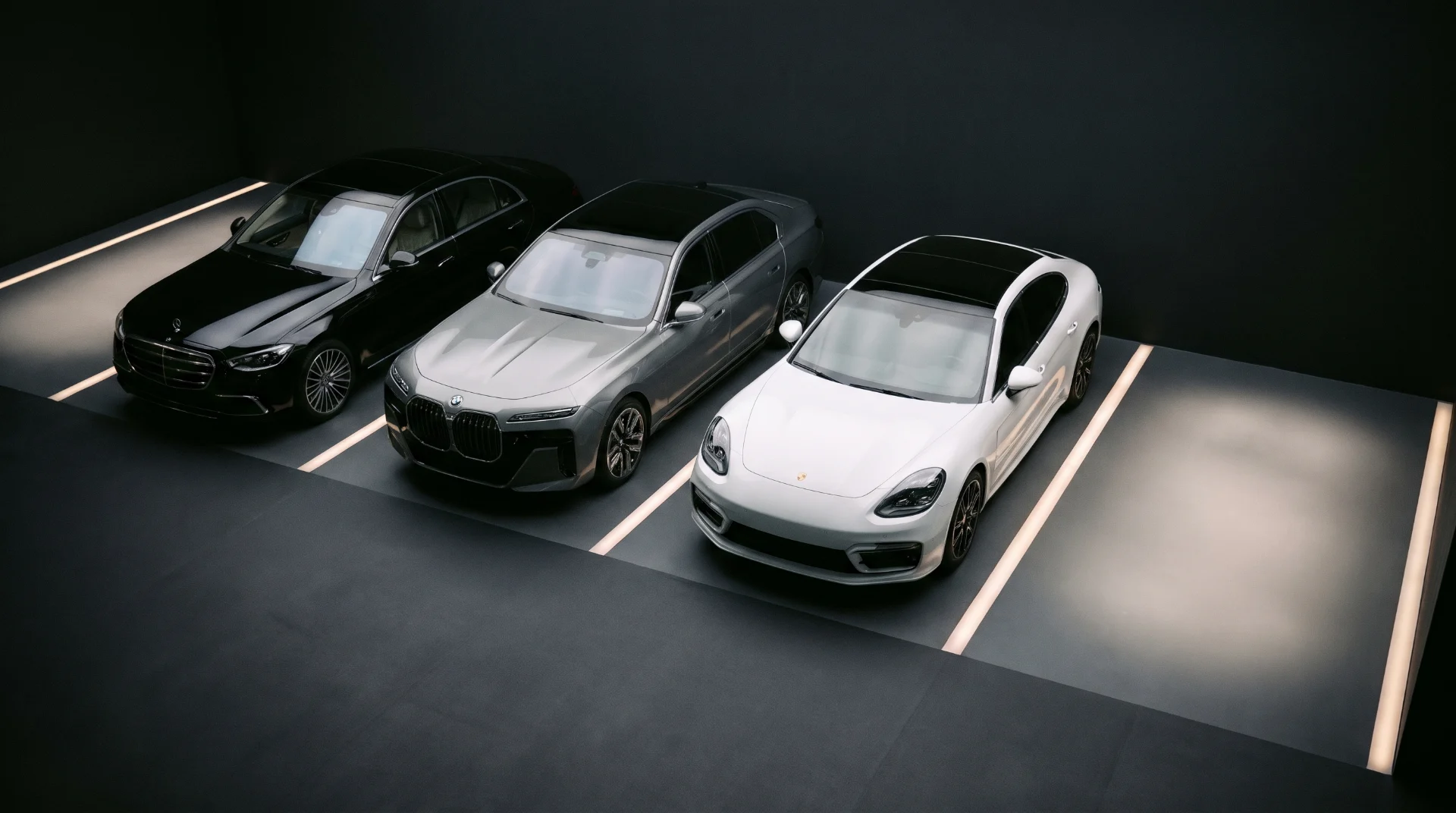 Illustration seen from above of a Mercedes-Benz S-Class, BMW i7 and Porsche Panamera beside an empty lit parking bay