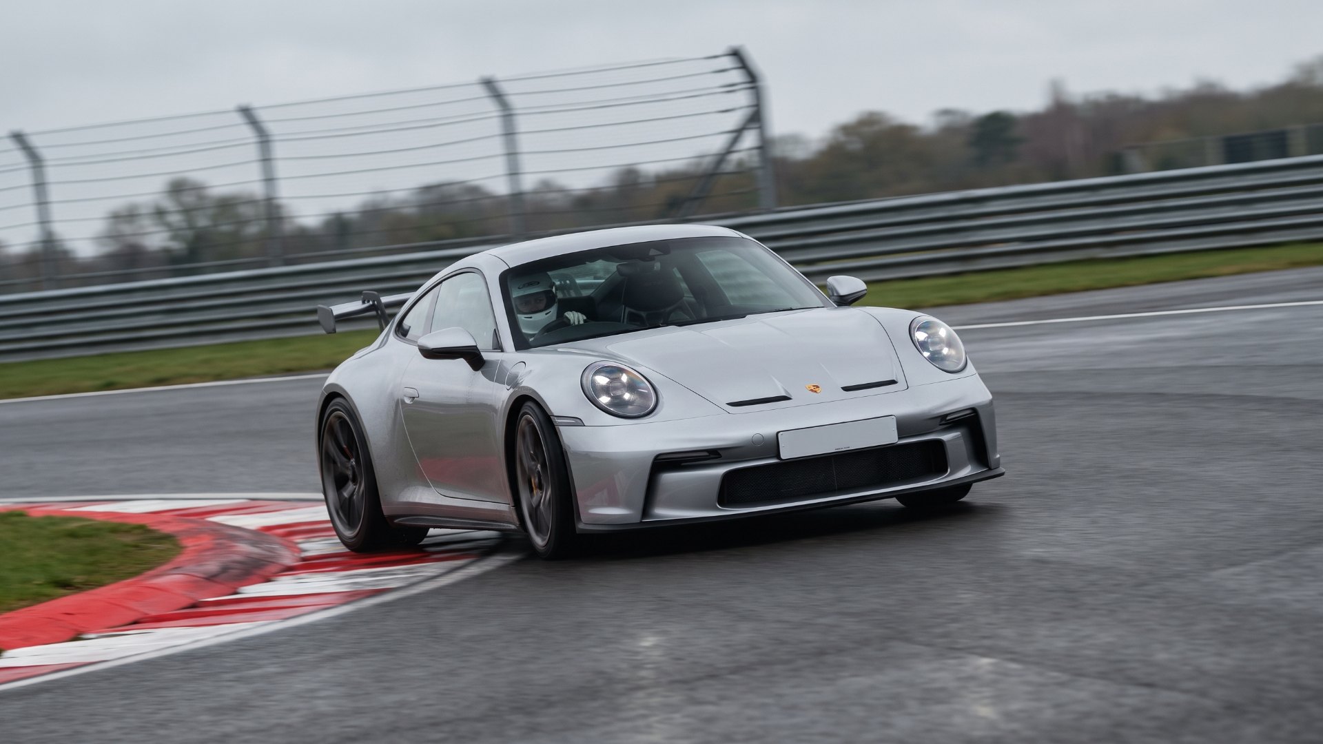 Silver Porsche 911 GT3 with rear wing cornering on a race circuit