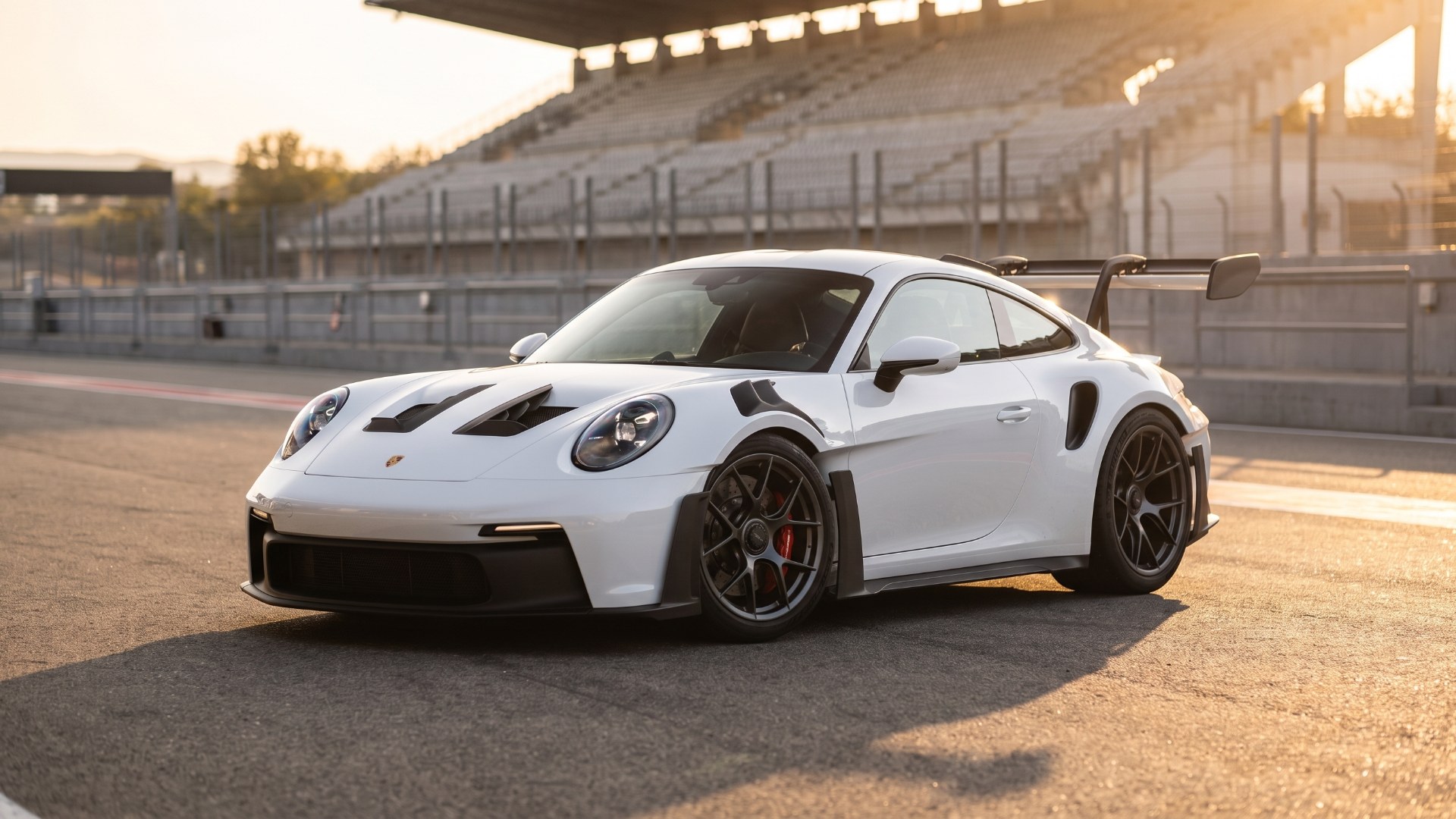 White Porsche 911 GT3 RS parked in a racetrack pit lane at golden hour