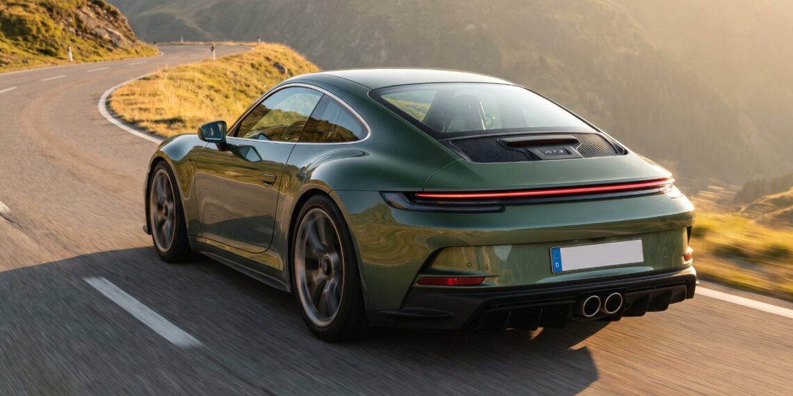 Green Porsche 911 GT3 Touring driving on an alpine road, seen from the rear