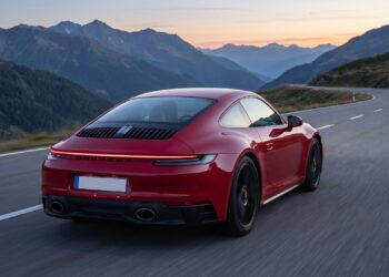 Red Porsche 911 coupe seen from the rear on a mountain road at dusk, its slatted engine lid and full-width light bar visible