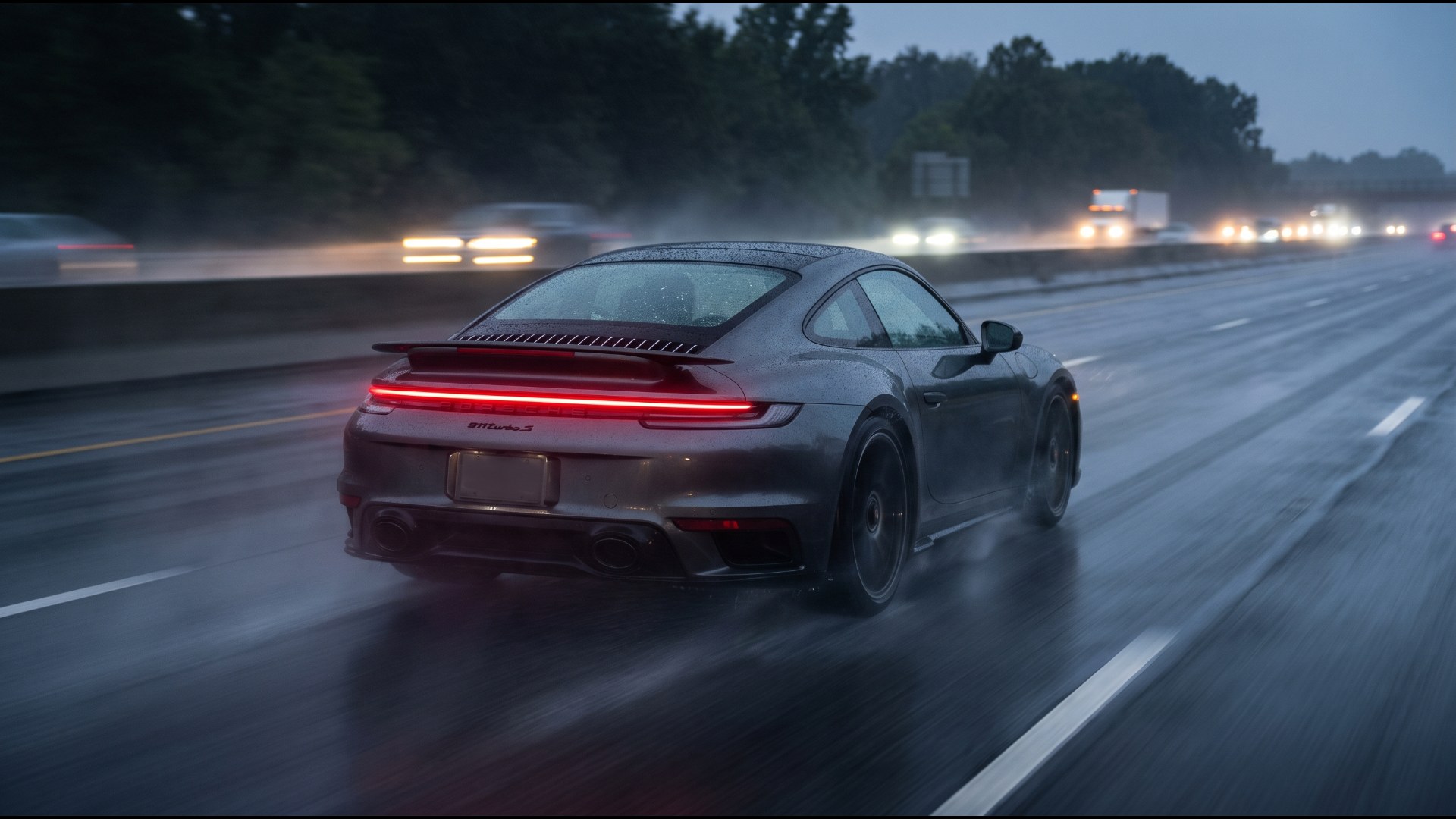 Dark gray Porsche 911 Turbo S throwing spray on a wet highway at dusk