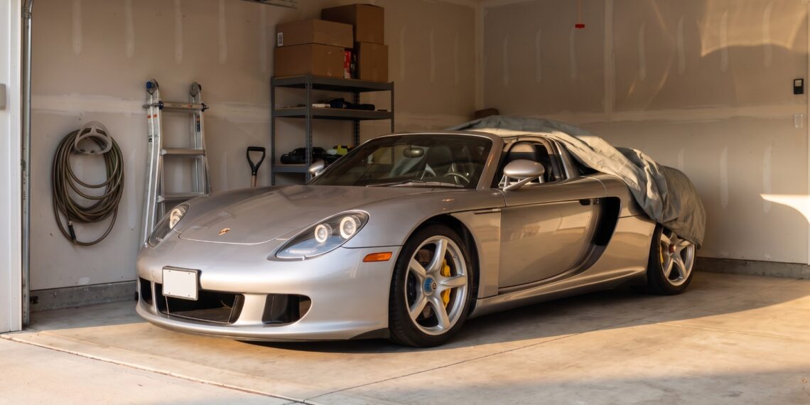 Silver Porsche Carrera GT in a suburban home garage with a car cover pulled halfway back