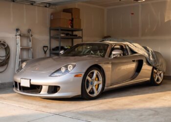 Silver Porsche Carrera GT in a suburban home garage with a car cover pulled halfway back