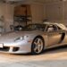 Silver Porsche Carrera GT in a suburban home garage with a car cover pulled halfway back