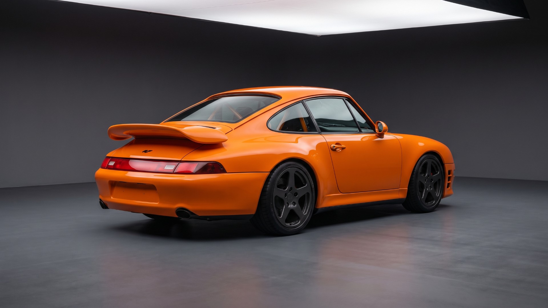 Rear three-quarter view of an orange air-cooled RUF-style 911 coupe with an integrated rear wing