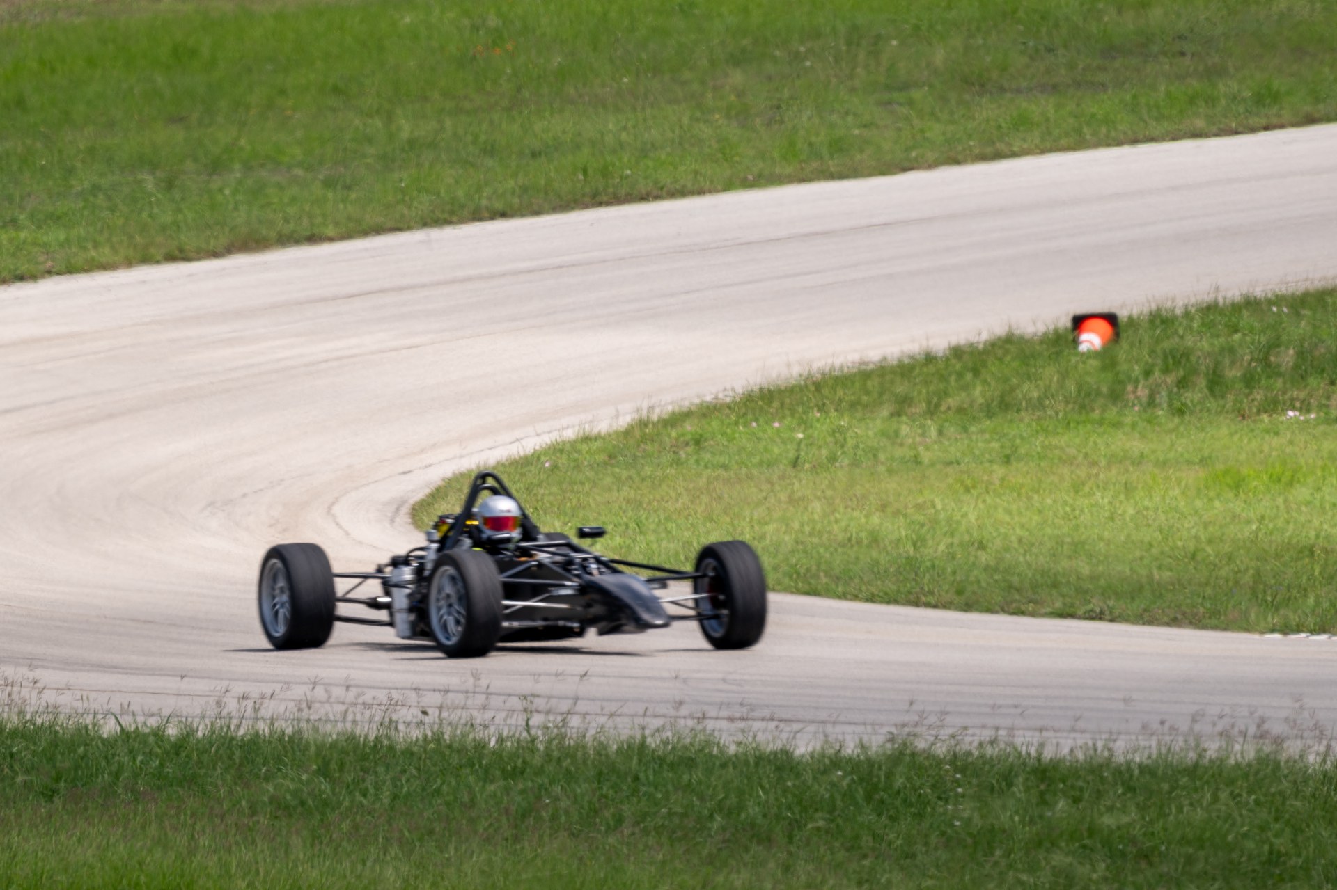 Bare RYN FP3 development chassis on four wheels cornering on a paved test circuit