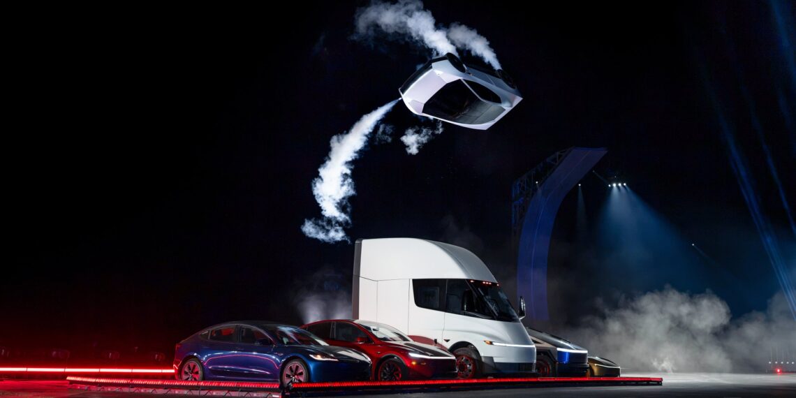 Tesla Roadster prototype airborne on thruster jets above a Tesla Semi and other Tesla vehicles at night