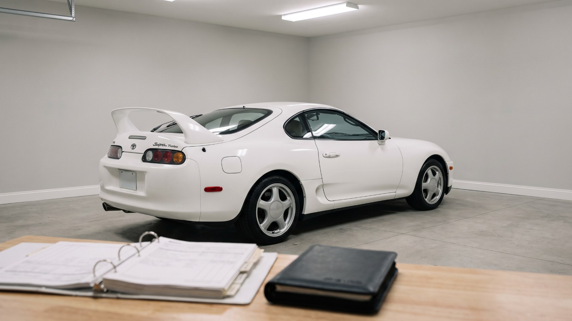Stock white Toyota Supra Turbo in a clean garage with a binder of service records in the foreground