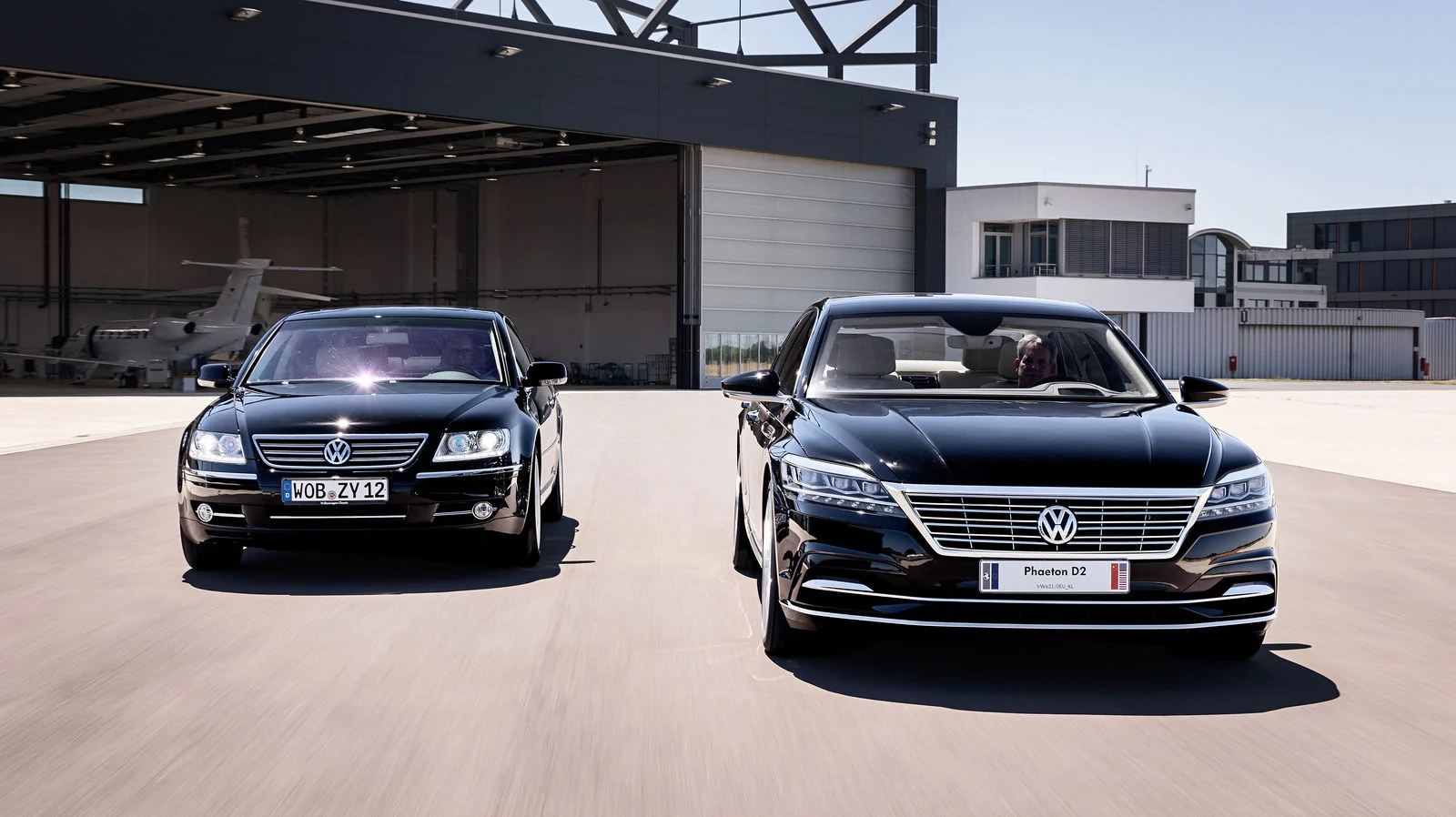 Two dark Volkswagen Phaeton sedans, the original and the unreleased Phaeton D2, outside a hangar