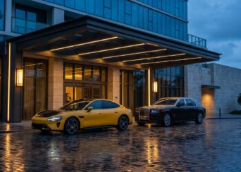Yellow Xiaomi SU7 Ultra parked beside a dark two-tone Rolls-Royce Phantom outside a hotel entrance at dusk