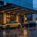 Yellow Xiaomi SU7 Ultra parked beside a dark two-tone Rolls-Royce Phantom outside a hotel entrance at dusk