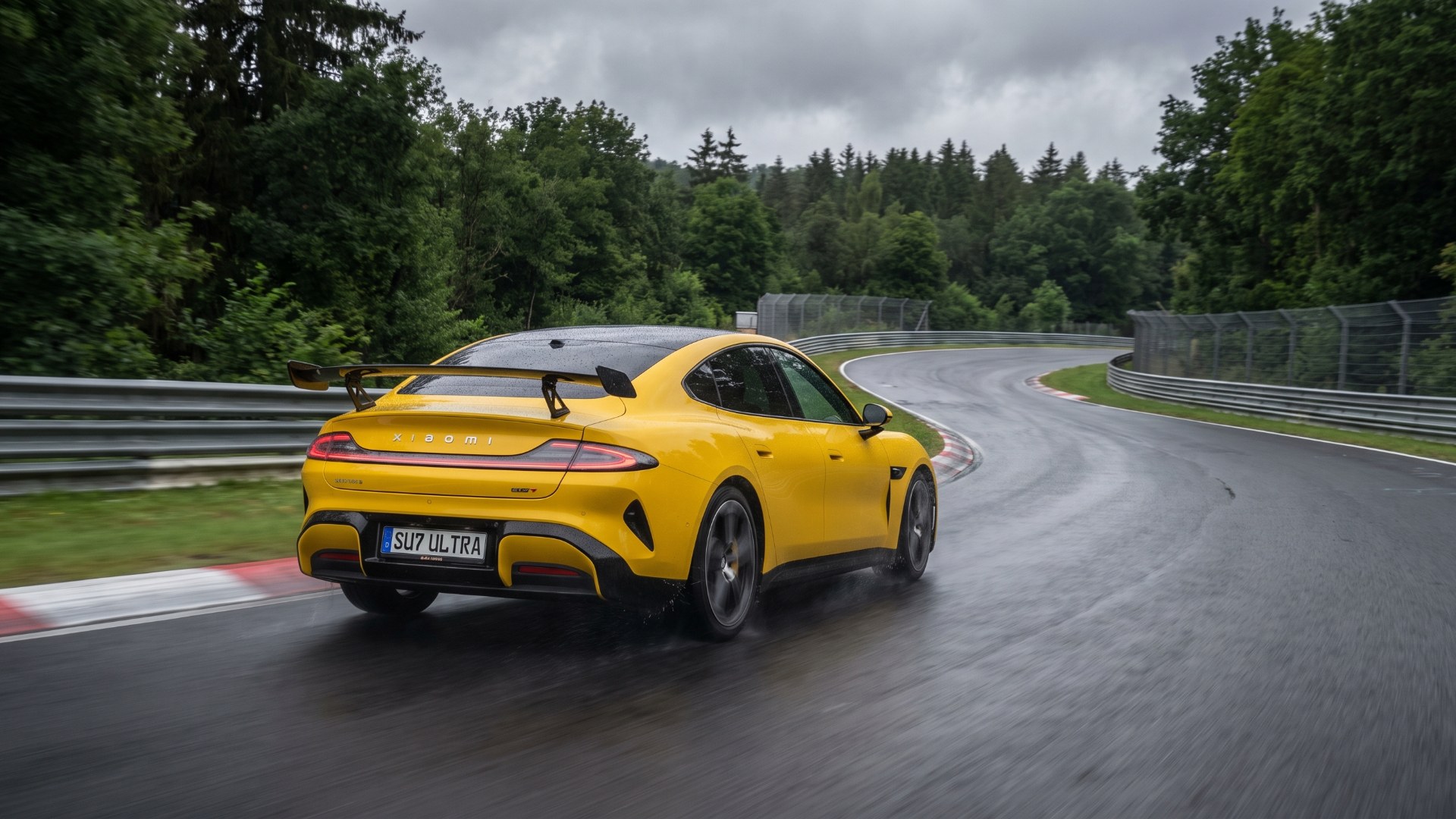 Yellow Xiaomi SU7 Ultra with a large rear wing cornering on a wet, tree-lined race circuit